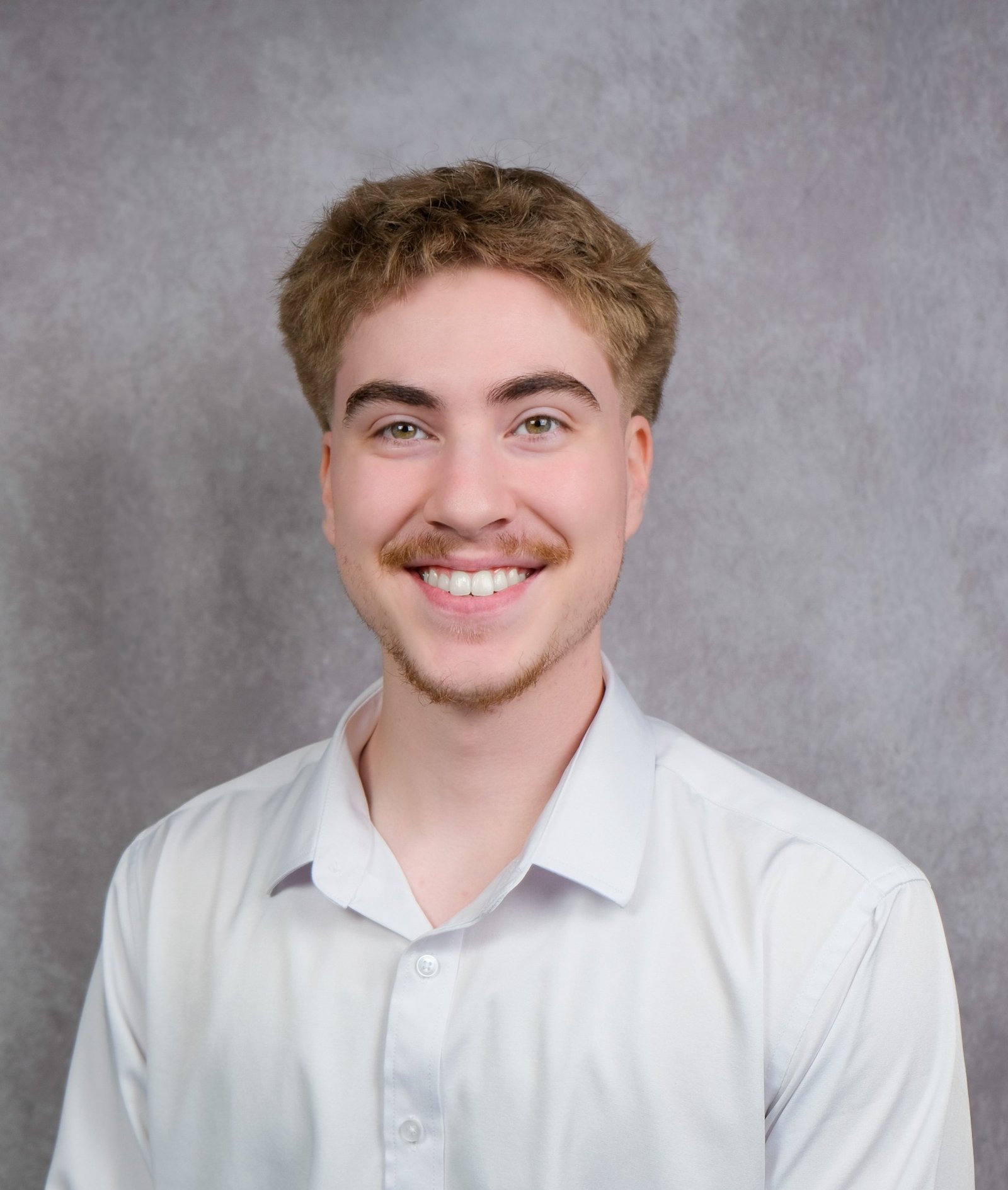 Kyle Odeen smiling, wearing a light shirt against a gray background